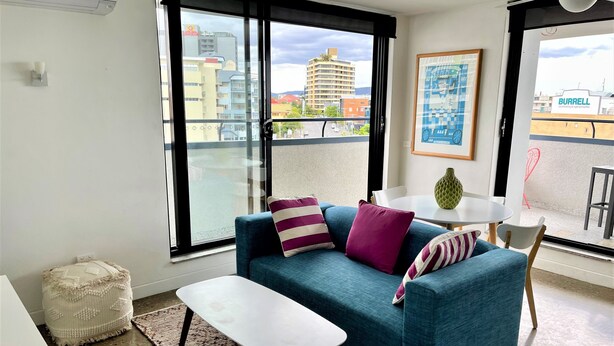 A modern living room with a blue sofa, a white coffee table, and a view of a cityscape through large windows.