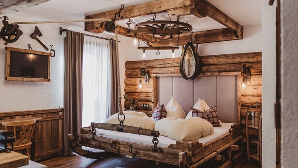 Un lit en bois rustique, doté d’une tête de lit, d’un banc en bois et d’un luminaire suspendu.