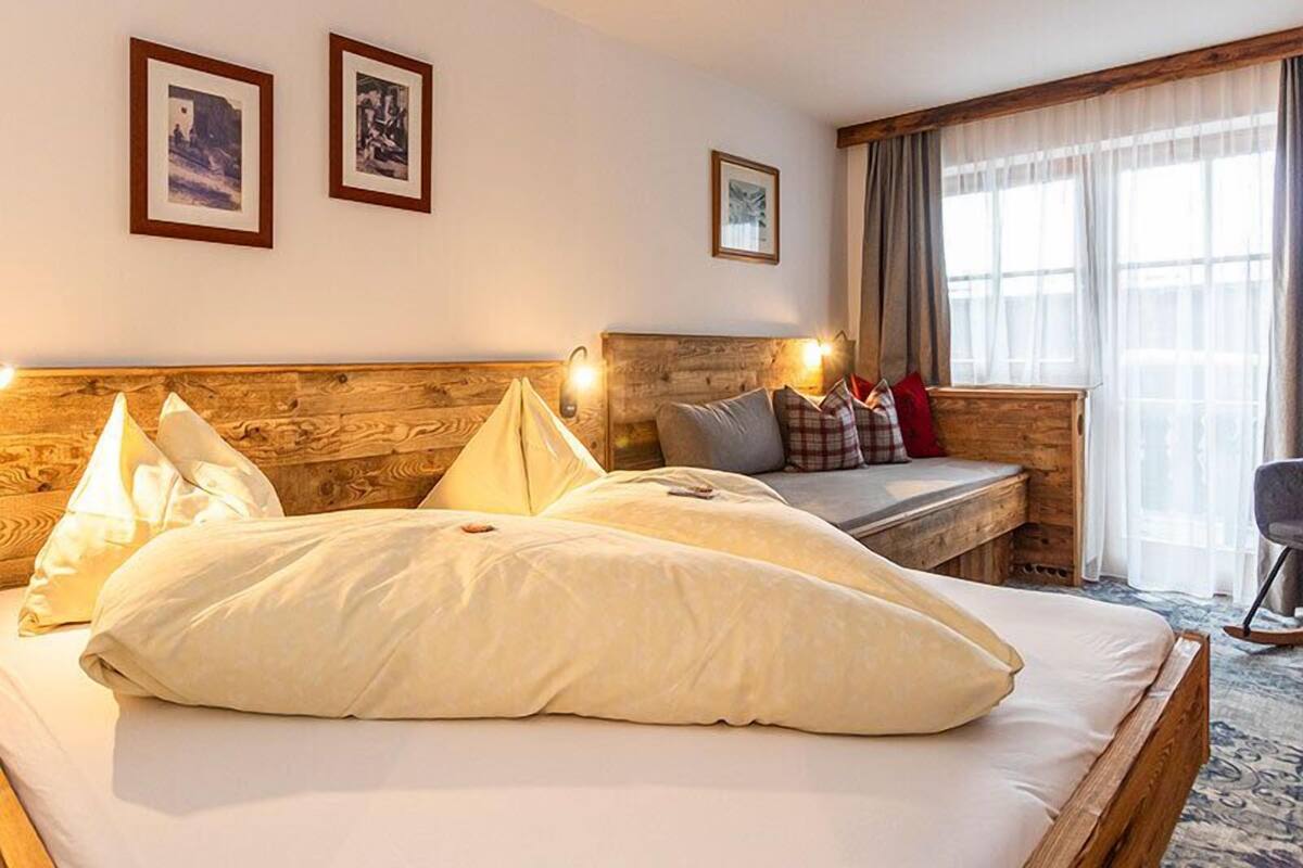 A hotel room with a wooden headboard, a bed with white bedding, a bench with cushions, and two framed pictures on the wall.