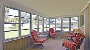 A sunroom with large windows, striped chairs, a small table, and a lamp.