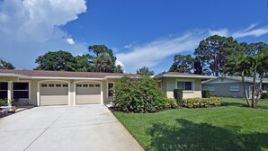 A two-story house with a garage, a well-maintained lawn, and mature trees in the background.