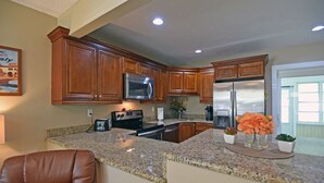 A kitchen with wooden cabinets, a stainless steel refrigerator, a microwave, and granite countertops.