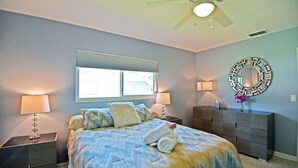 A bedroom with a bed, two bedside tables, a dresser, a ceiling fan, and a window with blinds.