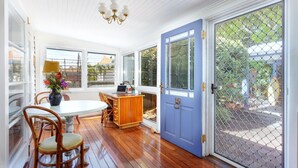 Une pièce avec un plancher en bois, une table à manger entourée de chaises, une porte bleue avec un panneau de verre et un lustre.