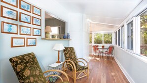 Une pièce baignée de lumière, avec un plancher en bois, une table à manger entourée de chaises et un mur orné d’œuvres d’art encadrées.