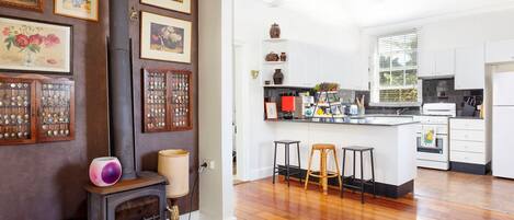 A modern kitchen with white cabinets, a central island, and a stove. There are framed pictures on the wall and a ceiling fan above.