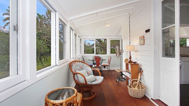 A sunroom with large windows, wicker furniture, a fan, and a small table. - Sunroom Cottage - 40A Witt Street (Tea Gardens)