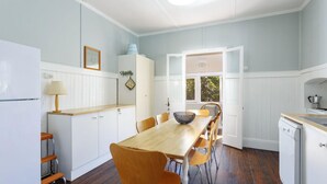 A kitchen with a wooden table, chairs, a refrigerator, and a stove. - Sunroom Cottage - 40A Witt Street (Tea Gardens)