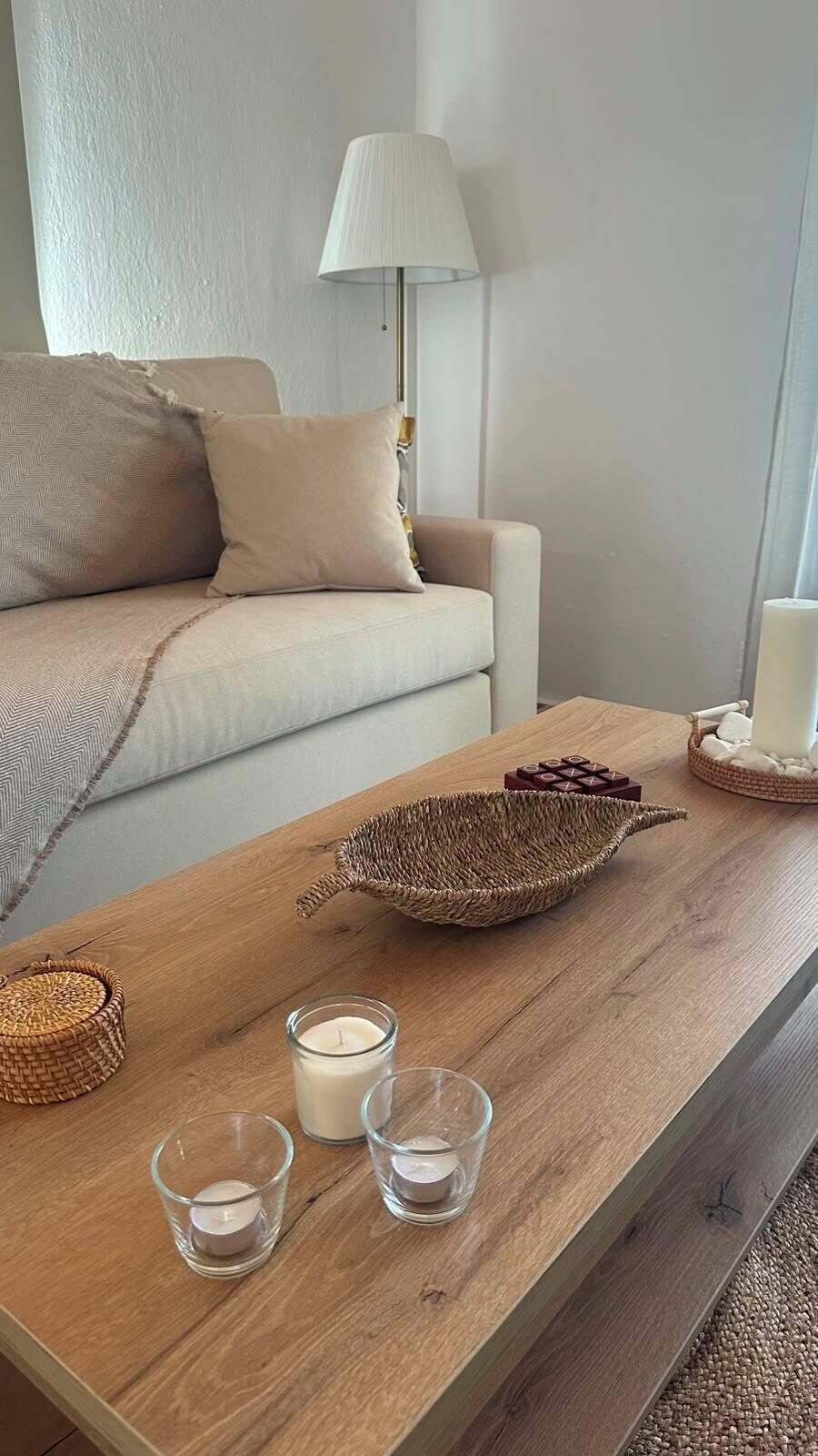 A wooden coffee table with a woven basket, two glass candle holders, and a white candle.