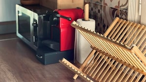 Una cocina con microondas, electrodoméstico rojo y un escurreplatos de madera.