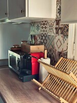 Una cocina con microondas, electrodoméstico rojo y un escurreplatos de madera.