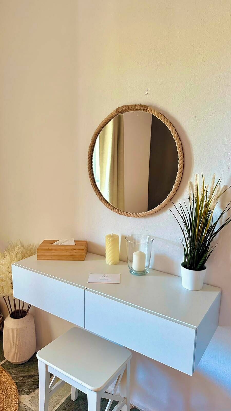 A white vanity with a round mirror, a candle, a tissue box, and a potted plant.