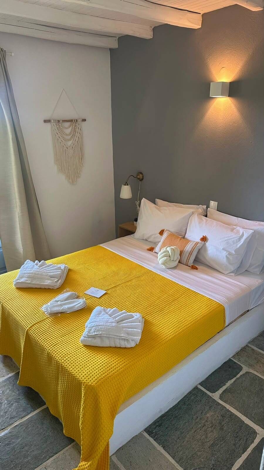Una habitación de hotel con una cama, almohadas, un edredón amarillo y una lámpara fijada a la pared.