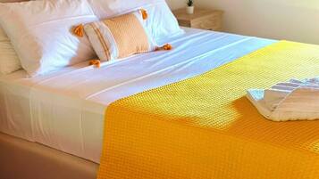 A bed with white bedding and a yellow throw blanket, a bedside lamp, and a small potted plant on a wooden nightstand.