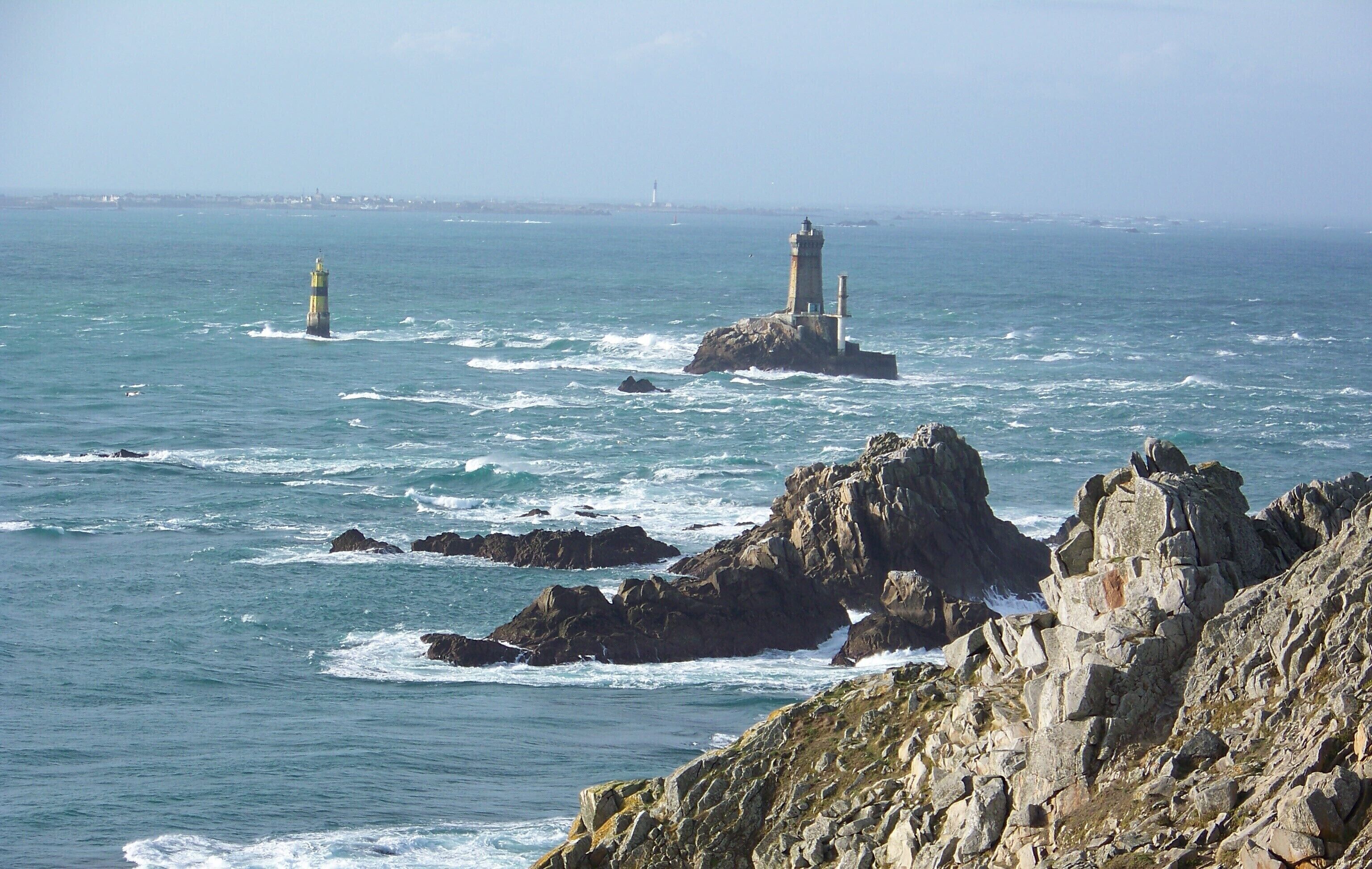 A coastal scene with rocky terrain and two lighthouses in the distance.