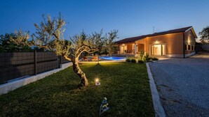 A modern house with a swimming pool, a well-maintained lawn, and a tree.