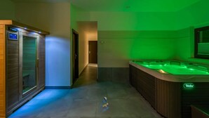 A spa area with a sauna, a massage room, and a hot tub, all under green lighting.