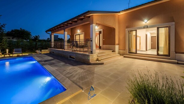 A modern house with a swimming pool, a covered patio, and a well-lit entrance.