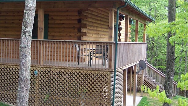 A log cabin with a balcony and a covered deck, surrounded by trees.