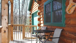 A wooden cabin with a porch, a table, and chairs.