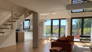 Ett rymligt vardagsrum med en trappa, en matplats med ett glasbord och stora fönster som erbjuder utsikt över grönområden.