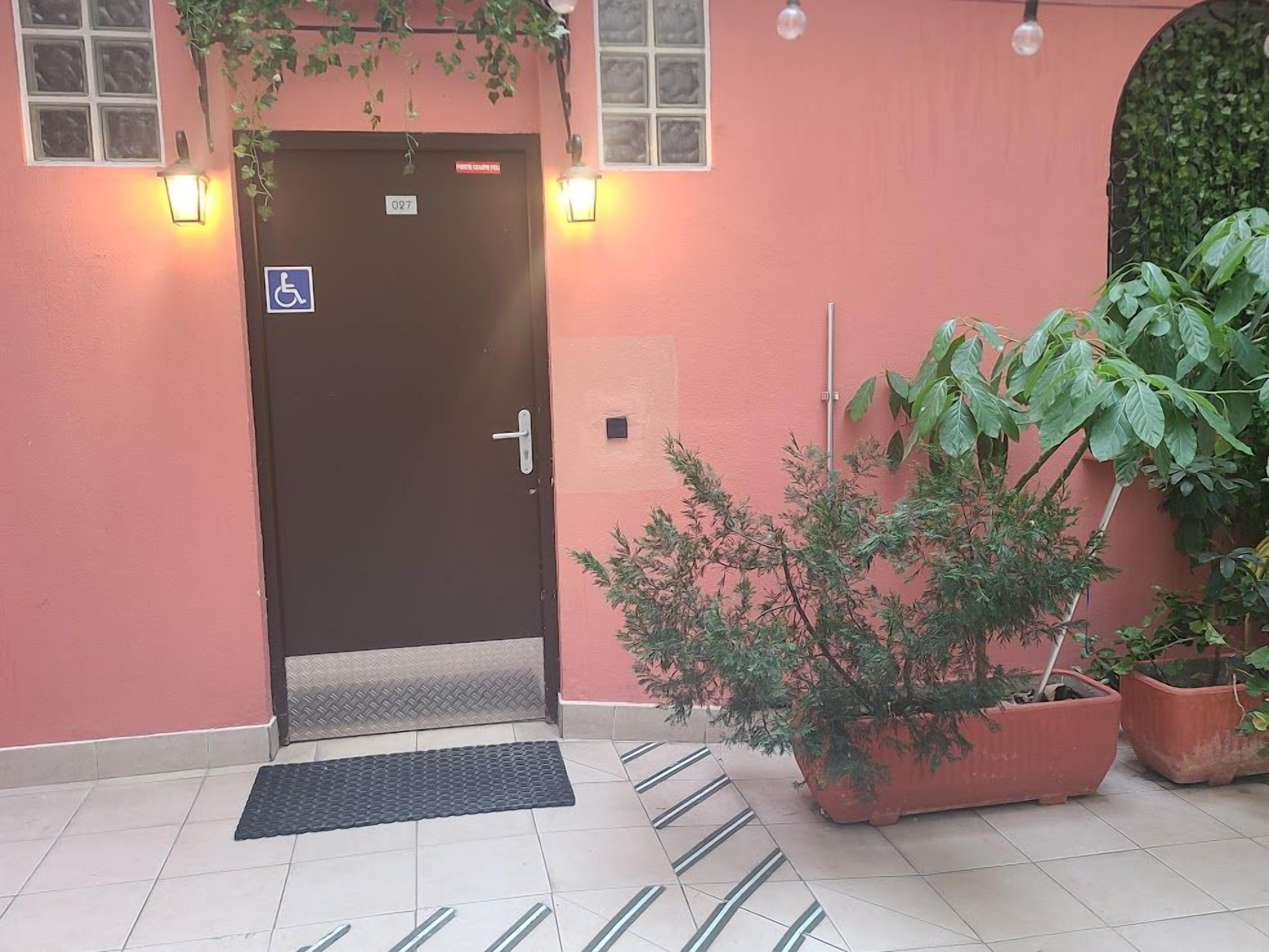 A hotel entrance with a wheelchair-accessible door, a mat at the entrance, and potted plants.