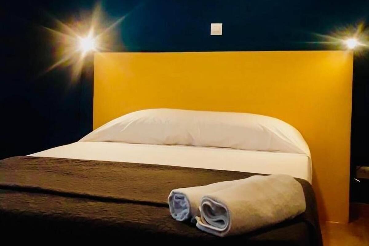 A hotel room with a bed, a headboard, and a wall switch.