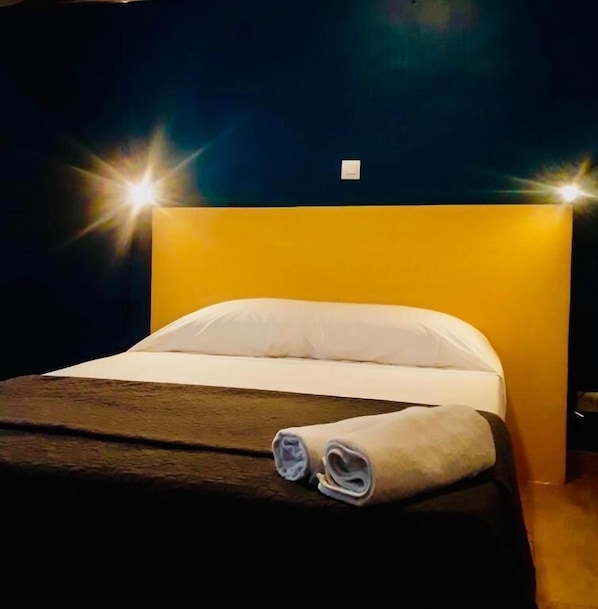 A hotel room with a bed, a headboard, and a wall switch.