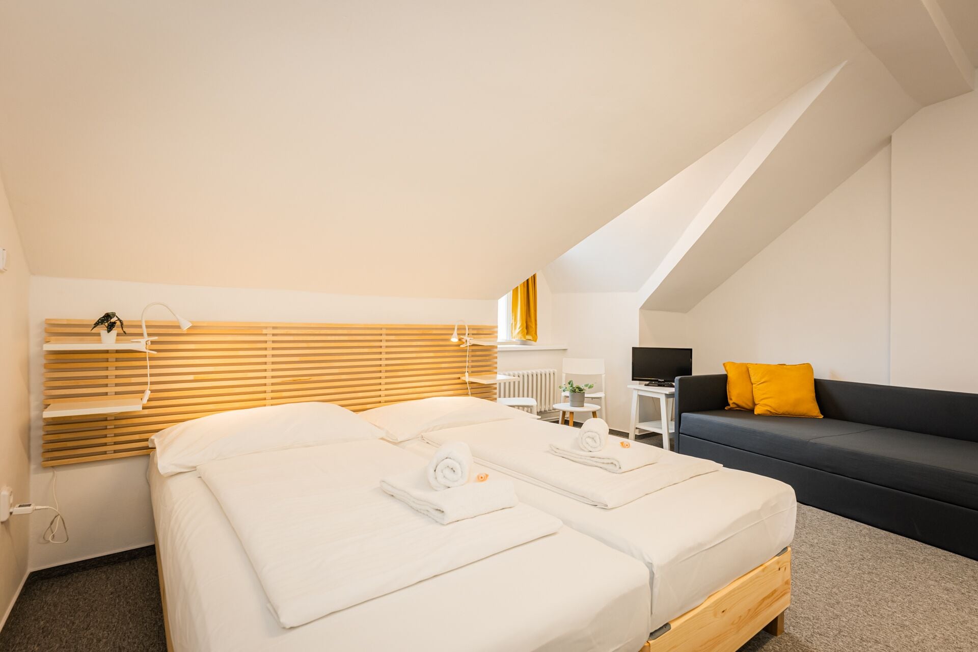 A modern hotel room with two beds, a desk, a sofa, and a TV.