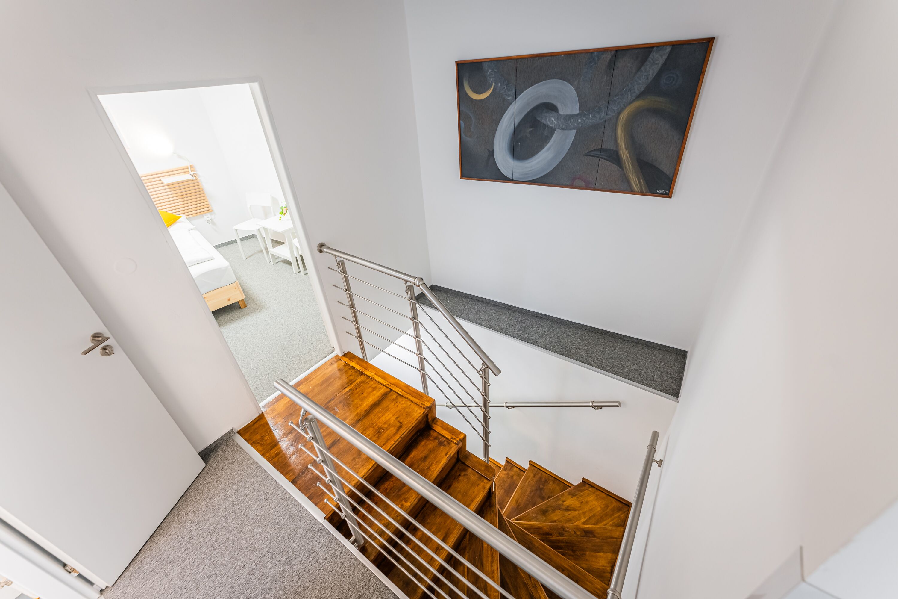 Una habitación de hotel moderna con una escalera de madera, un cuadro en la pared y vistas a la habitación contigua.