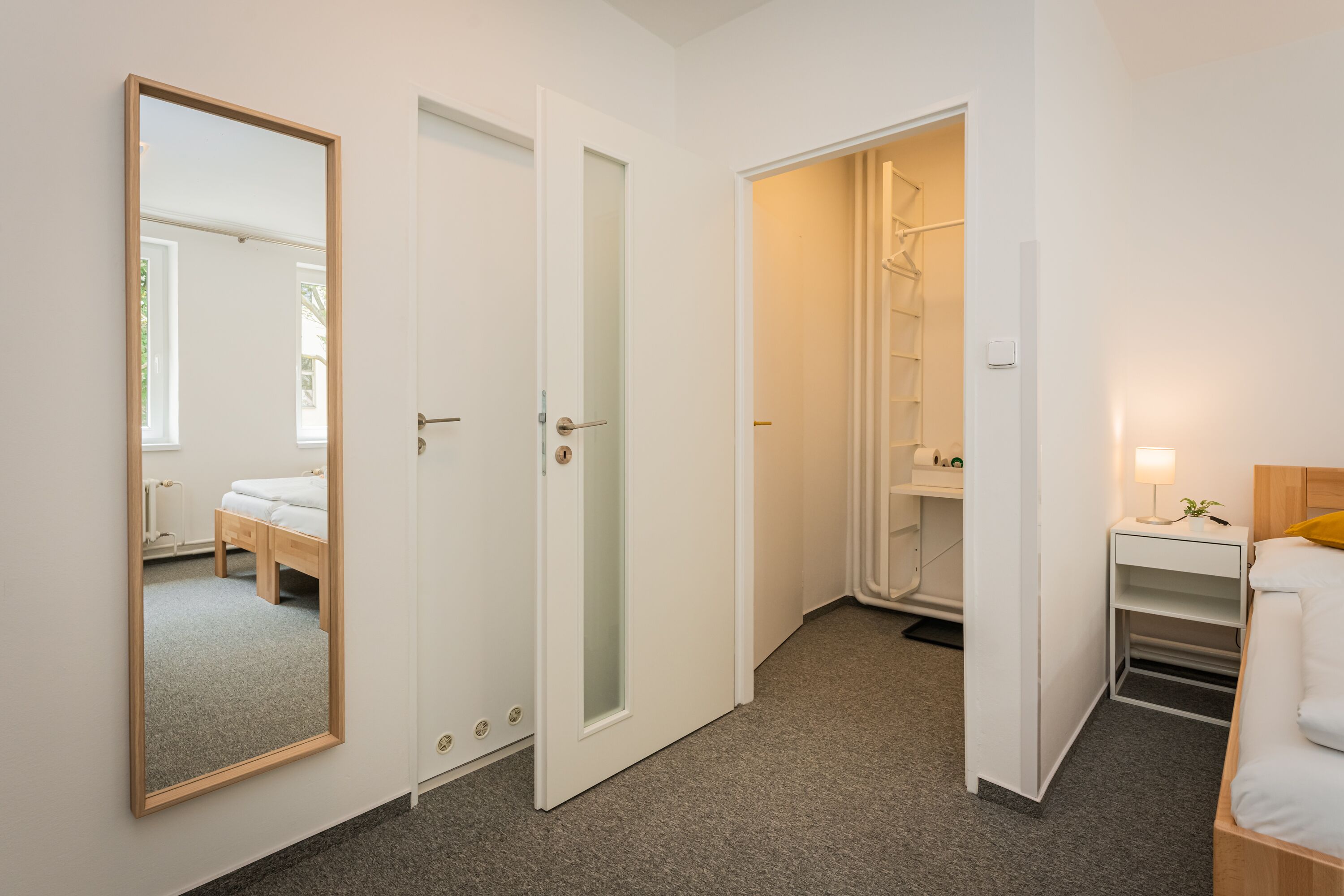 A hotel room with a bed, a bedside table with a lamp, a wardrobe, and a mirror.