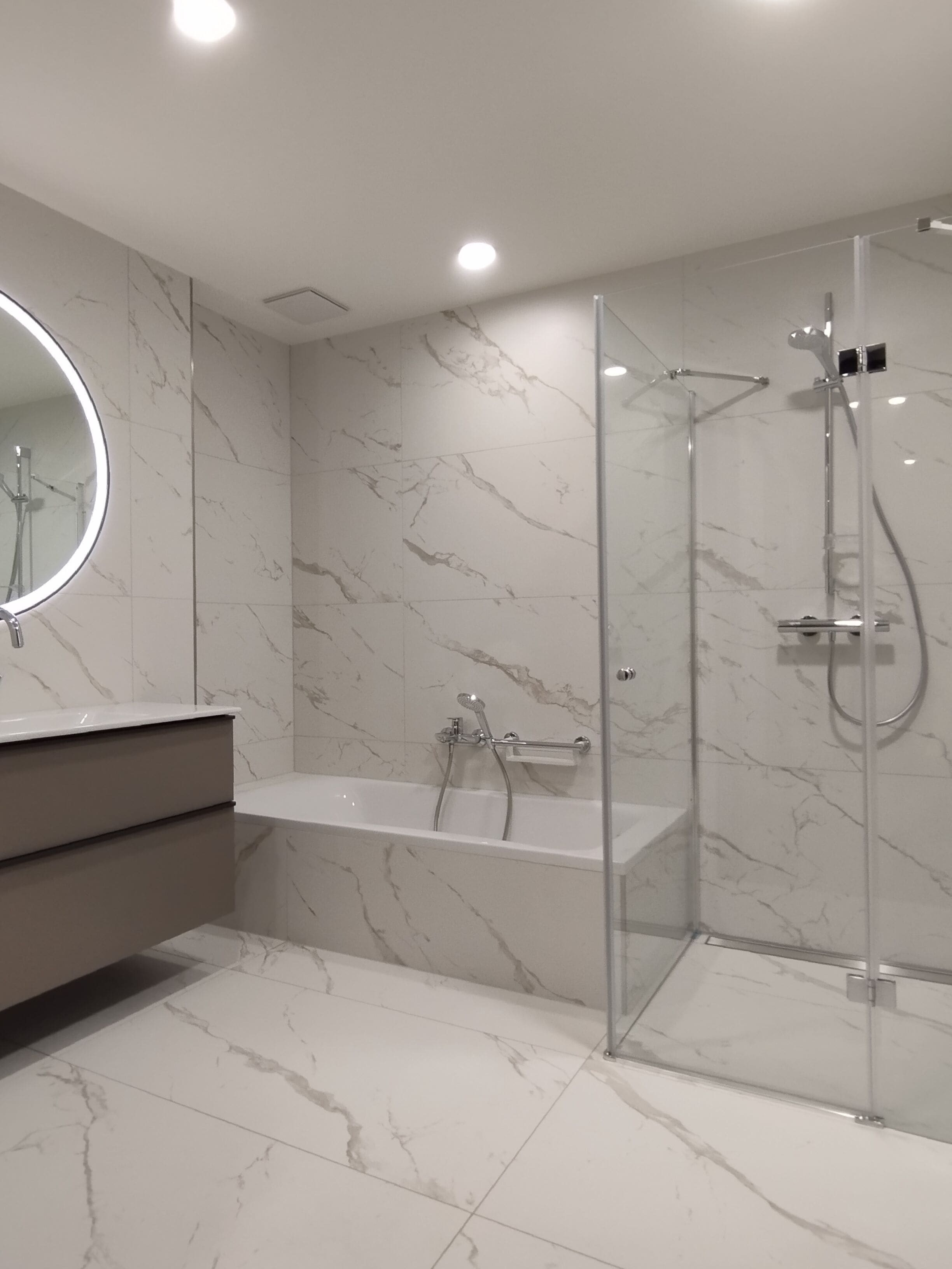Un baño moderno con ducha de vidrio, una bañera independiente y un espejo redondo sobre el lavamanos.