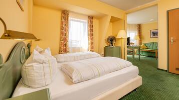 Een hotelkamer met een bed, een bureau, een stoel, een lamp, een klok en een deur.