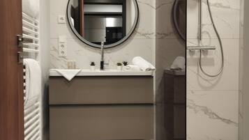 Une salle de bain moderne avec un sol en marbre, un miroir rond, un lavabo avec une serviette et un espace douche.
