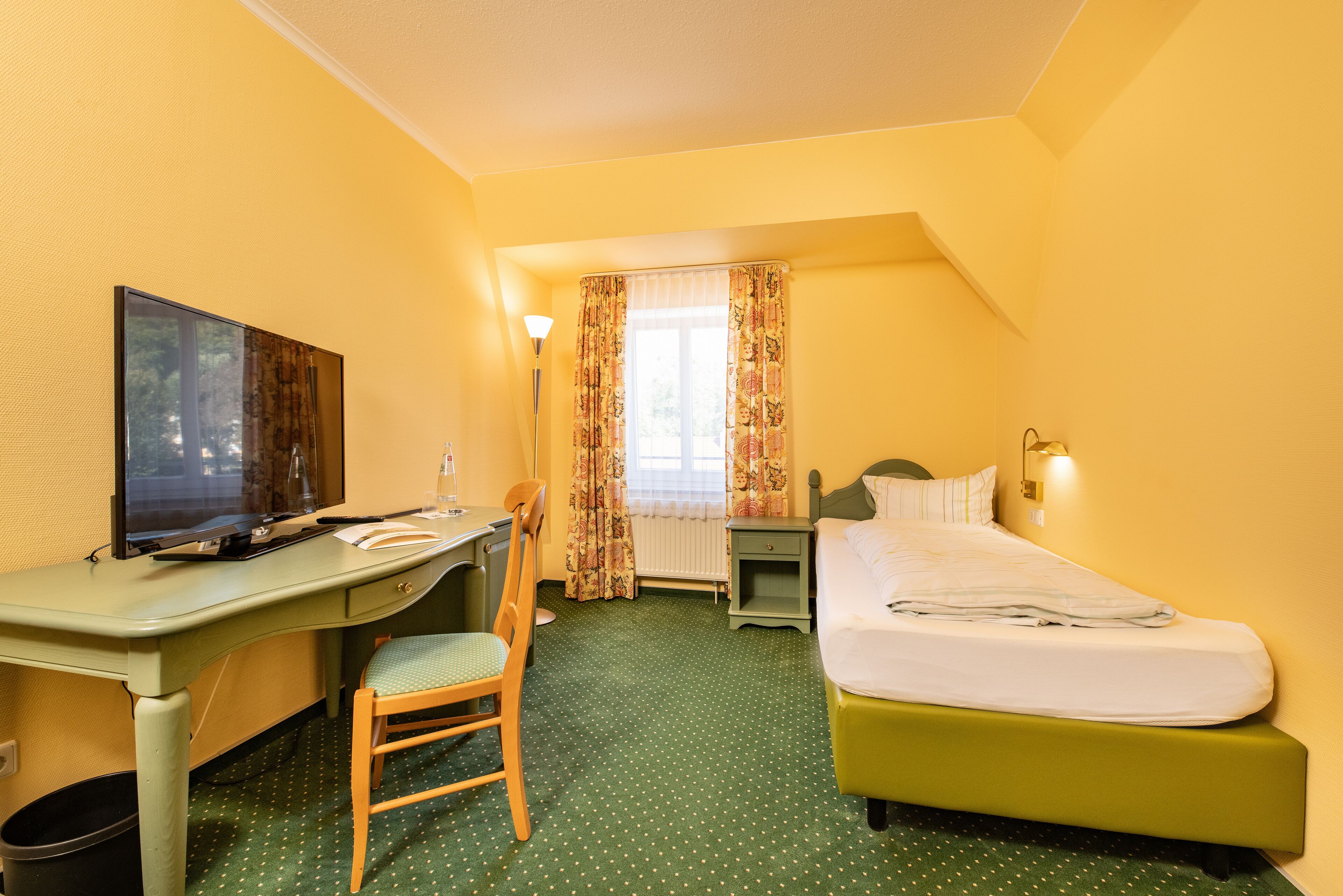 A hotel room with a desk, chair, bed, and a window with curtains.