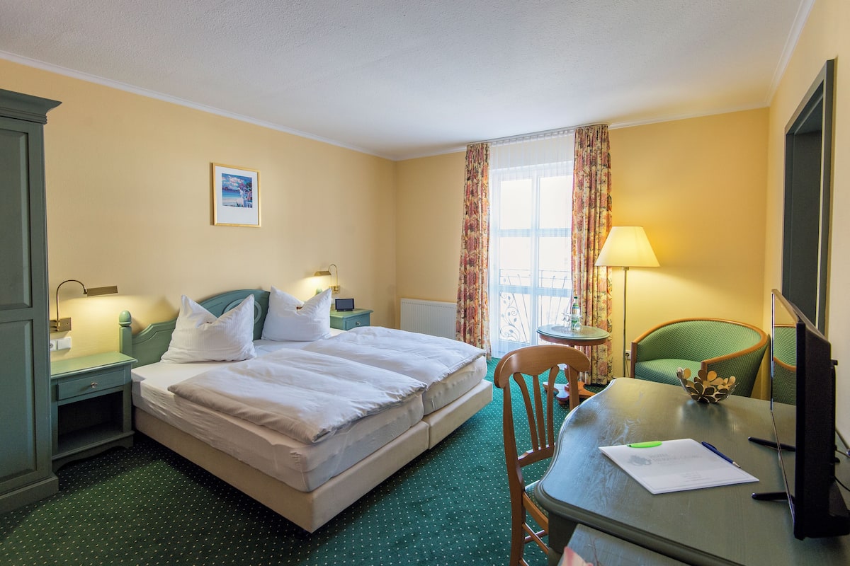Habitación de hotel con cama, escritorio, silla, lámpara y ventana con cortinas.