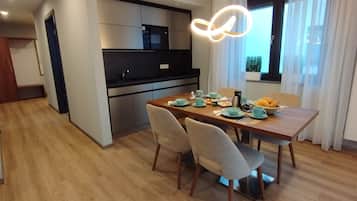 Una cocina moderna con electrodomésticos integrados, un comedor con mesa y sillas de madera, y vistas al exterior a través de un ventanal.