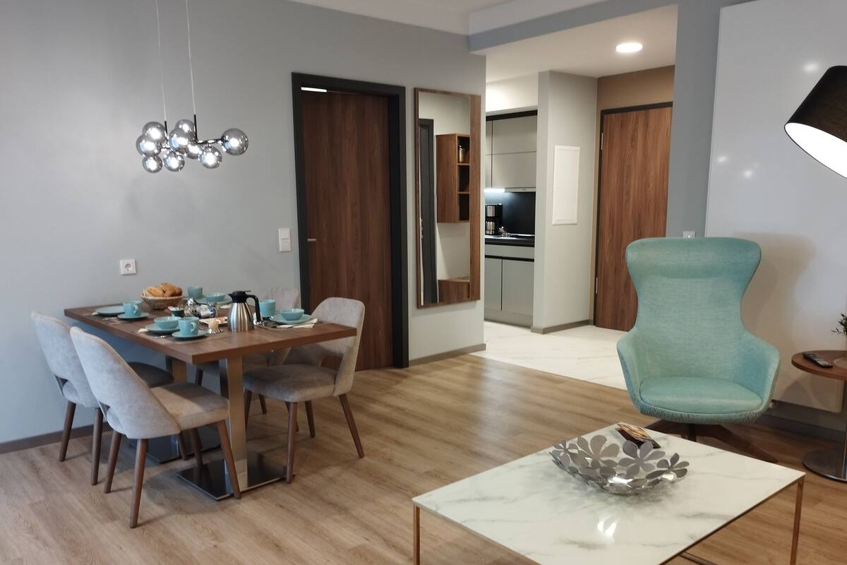 Una sala de estar moderna con comedor, una cocina al fondo y un sillón color turquesa.