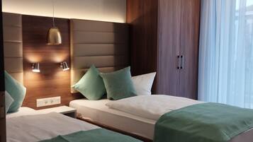 A hotel room with two beds, wooden headboards, and a large window with sheer curtains.