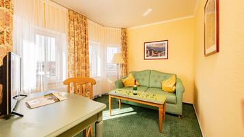 Een hotelkamer met een groene bank, een houten tafel, een lamp en een ingelijst schilderij aan de muur.