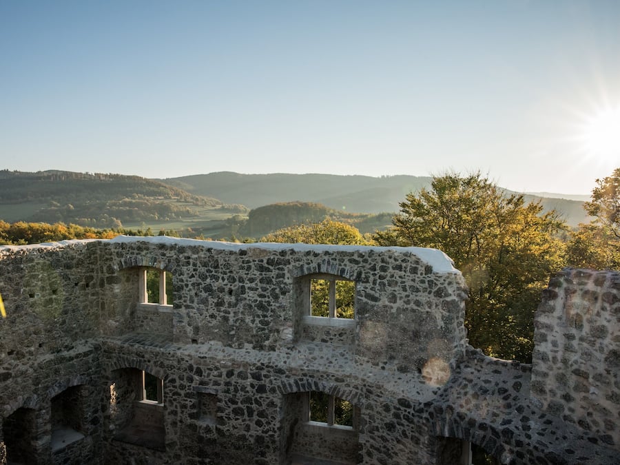 An ancient stone structure with arched windows and a view of rolling hills in the background.