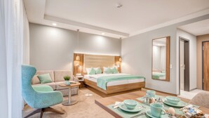 Una habitación de hotel moderna con una cama grande, un sofá, una mesa de comedor con desayuno servido y un espejo amplio.