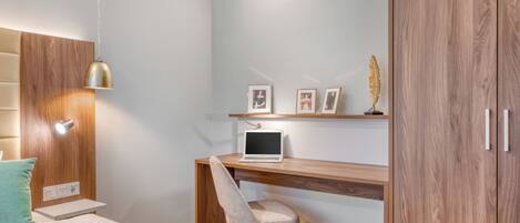 Een slaapkamer met een bed, een bureau met een laptop, een stoel, een plank met foto’s en een kledingkast.