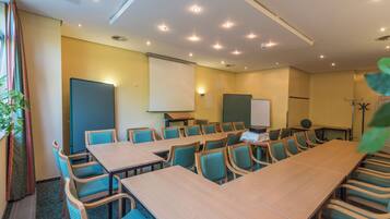 A conference room with a long table, multiple chairs, a projector screen, and a whiteboard.