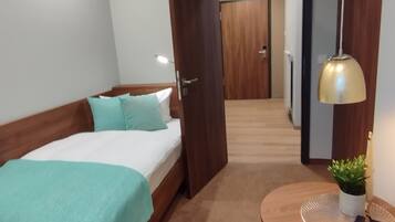 Quarto com cama, mesa redonda com uma planta e corredor que leva a uma porta.