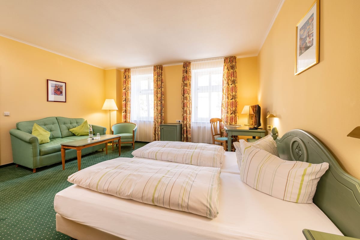 Una habitación de hotel con dos camas, un sofá verde, una mesita y una silla.