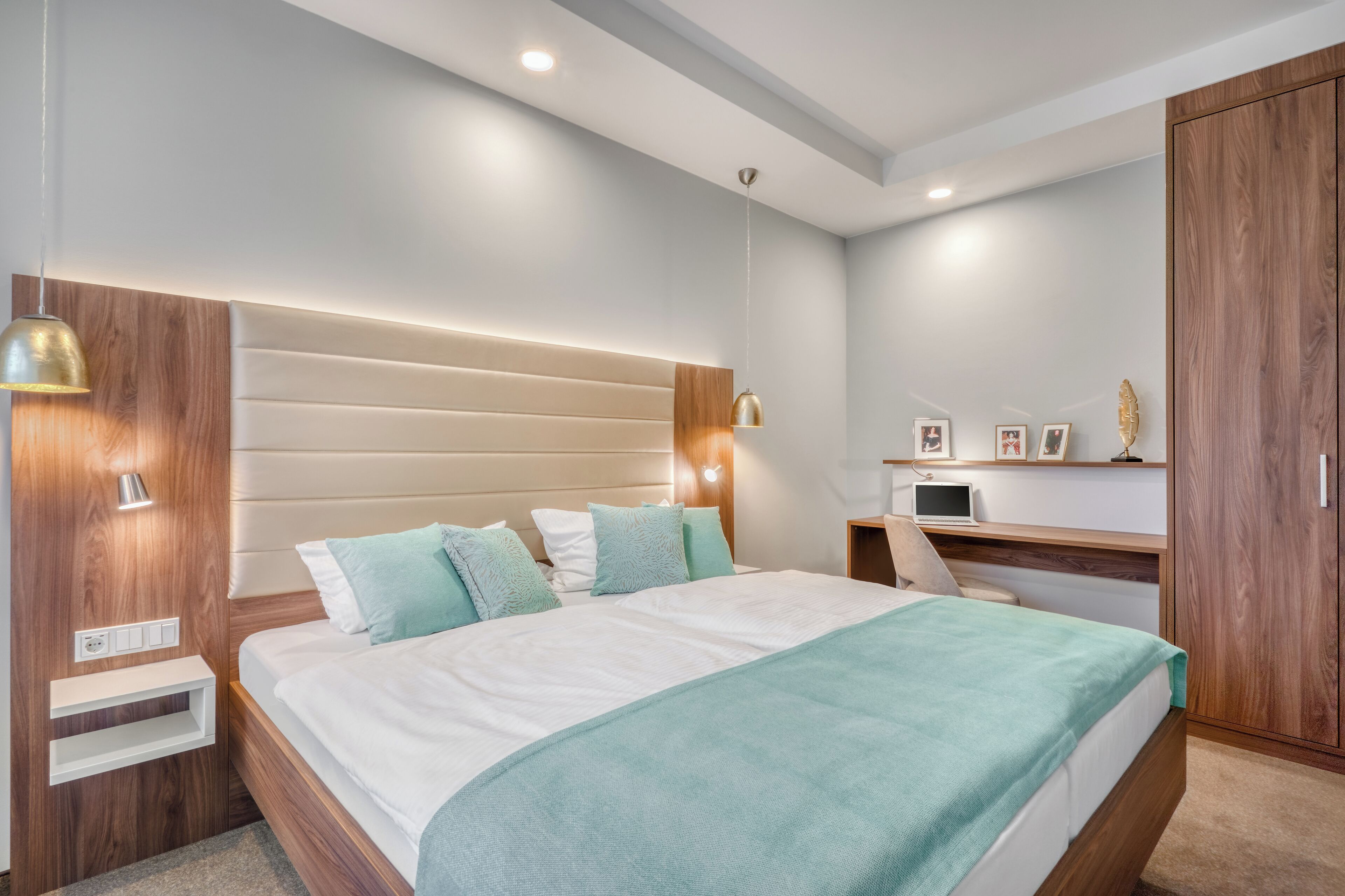 Un dormitorio moderno con una cama grande, lámparas de noche, un armario de madera y un escritorio pequeño con una computadora.