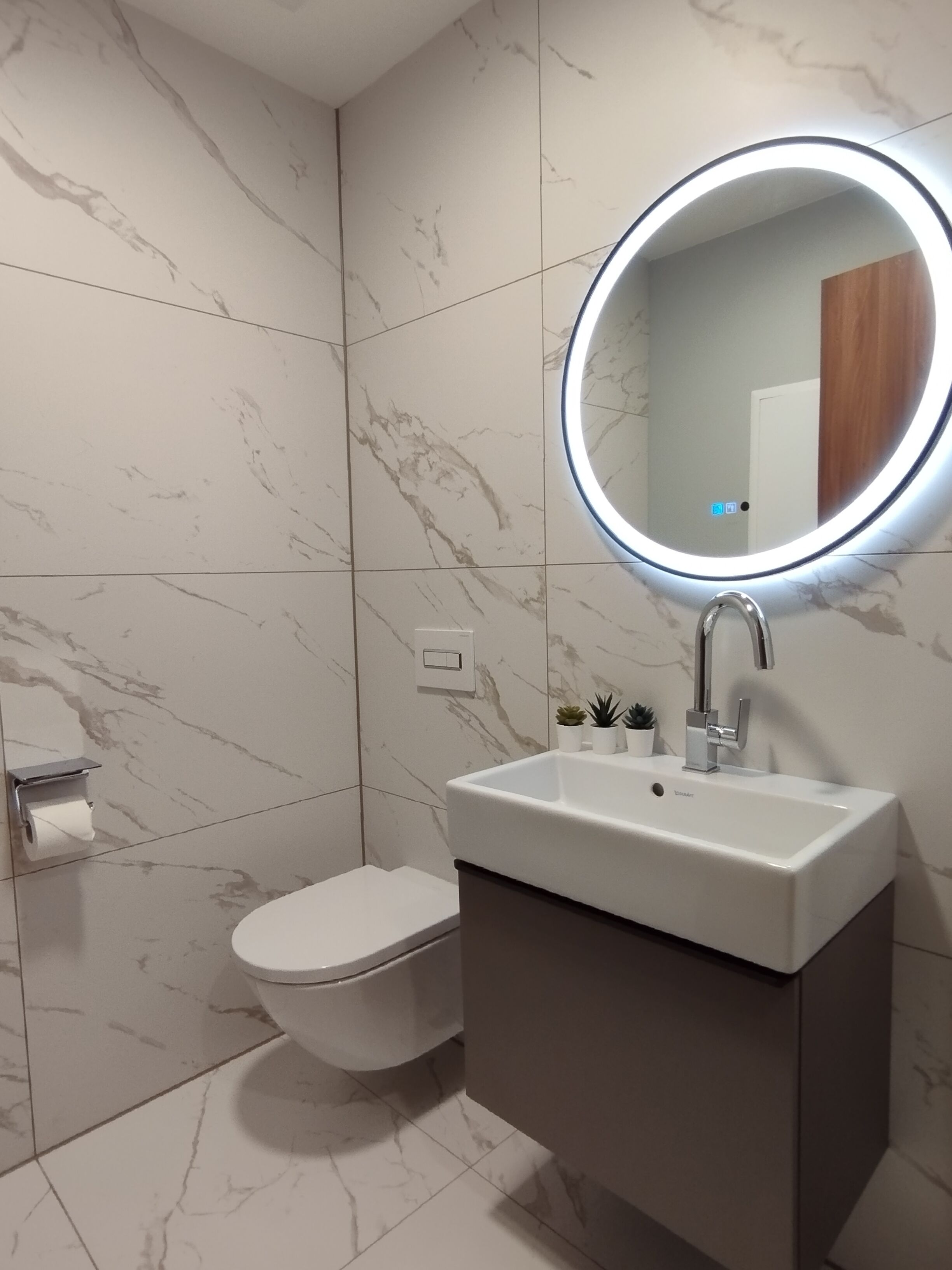 A modern bathroom with a white toilet, a sink with a mirror, and a marble-tiled wall.
