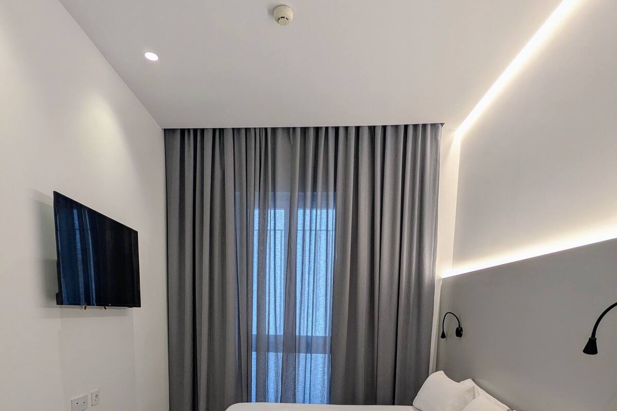A modern bedroom with a bed, a TV mounted on the wall, and a window with curtains.