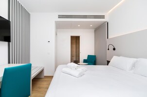A modern hotel room with a neatly made bed, a desk with a chair, and a small round table.